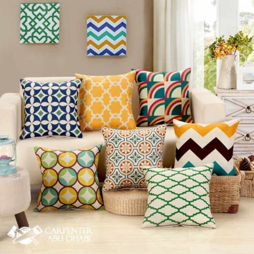 Colorful decorative pillows with geometric patterns arranged on a beige sofa and floor.