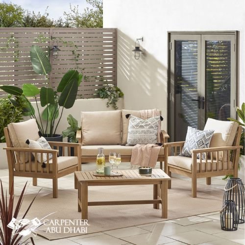 Cozy outdoor patio with wooden furniture, neutral cushions, greenery, soft lighting, and a relaxing ambiance.