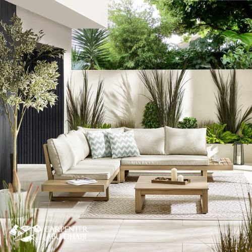Modern outdoor patio with wooden furniture, neutral cushions, greenery, and decorative accents.