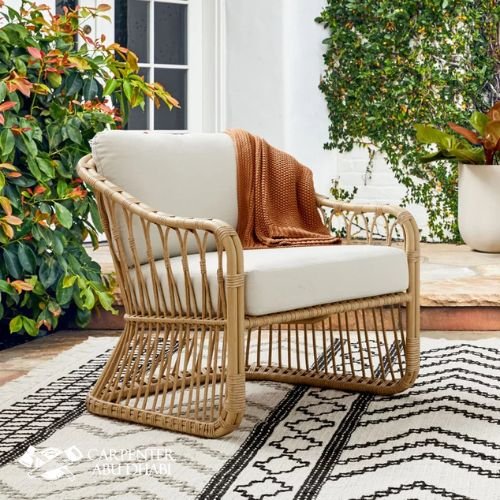 Wicker patio chair with white cushions, brown throw, and outdoor greenery.