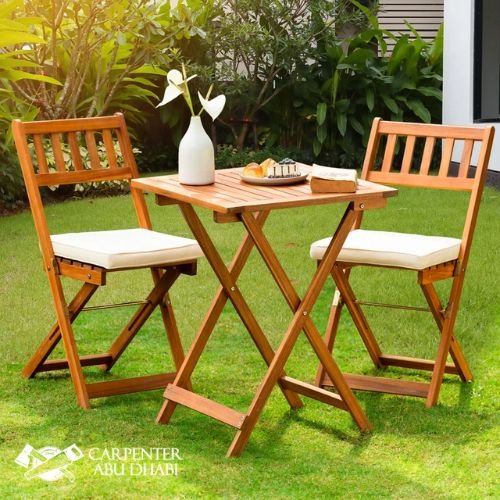 Wooden bistro set, foldable chairs, small table, white cushions, green grass, outdoor dining.