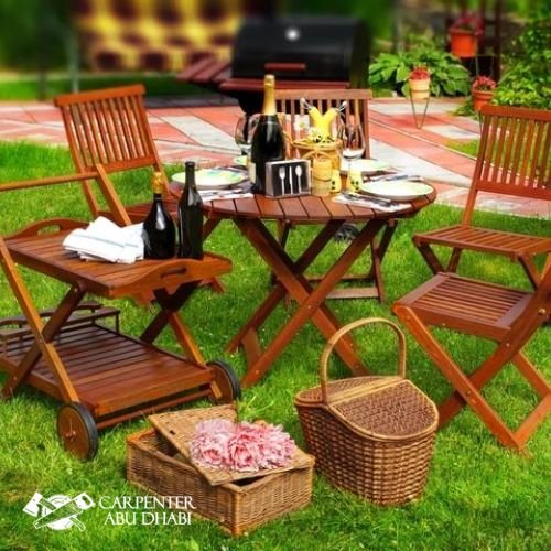 Wooden outdoor dining set with wine, picnic baskets, and greenery.