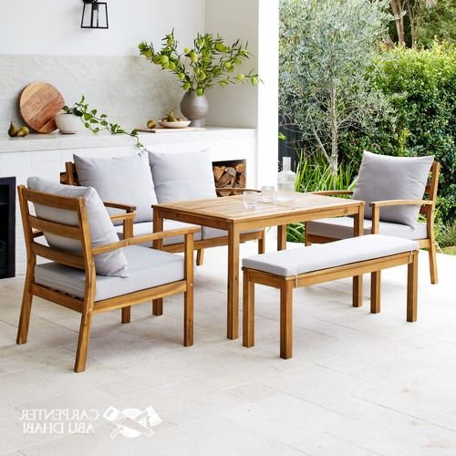 Wooden outdoor furniture with gray cushions, surrounded by greenery and decor.
